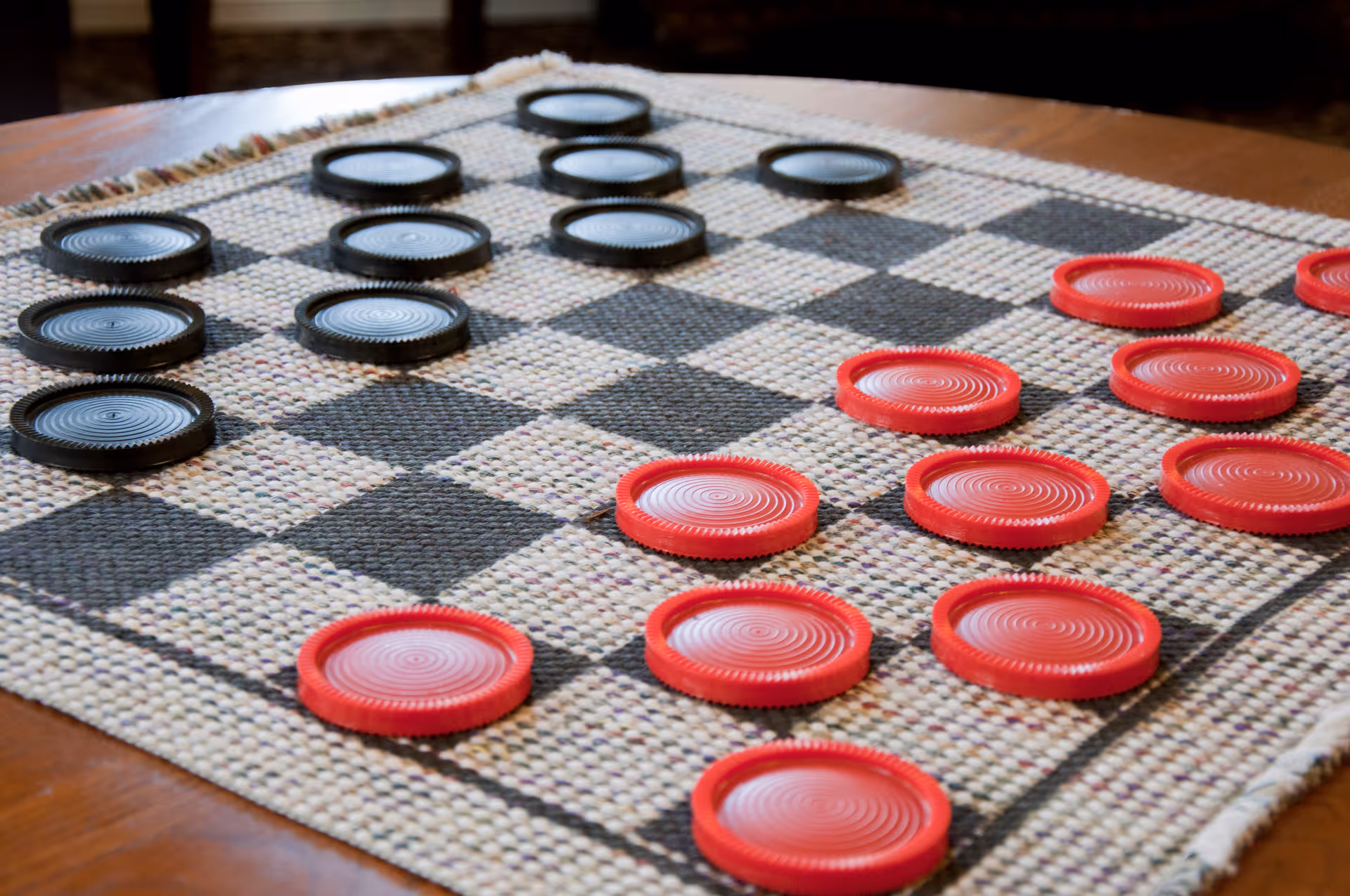 Close-up of a checkers game in progress on a woven fabric board with black and red round pieces arranged on the squares.