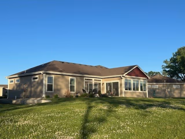 Single-story building with beige siding and a brown roof, surrounded by a green lawn with small white flowers under a clear blue sky.