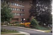 Brick senior living building with landscaped entrance, trees, and curved sidewalk.