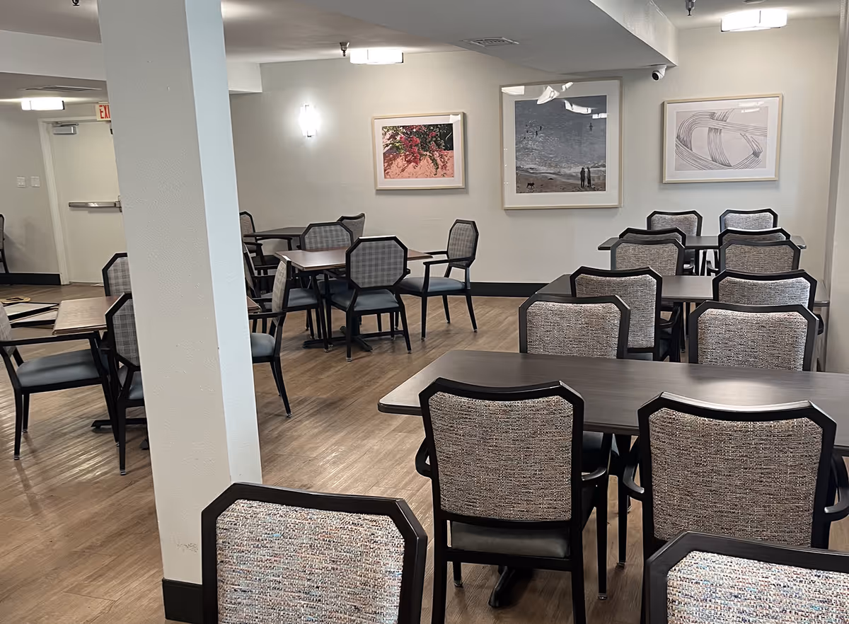 Empty dining room with multiple dark wood tables and upholstered chairs and framed artwork on the walls.