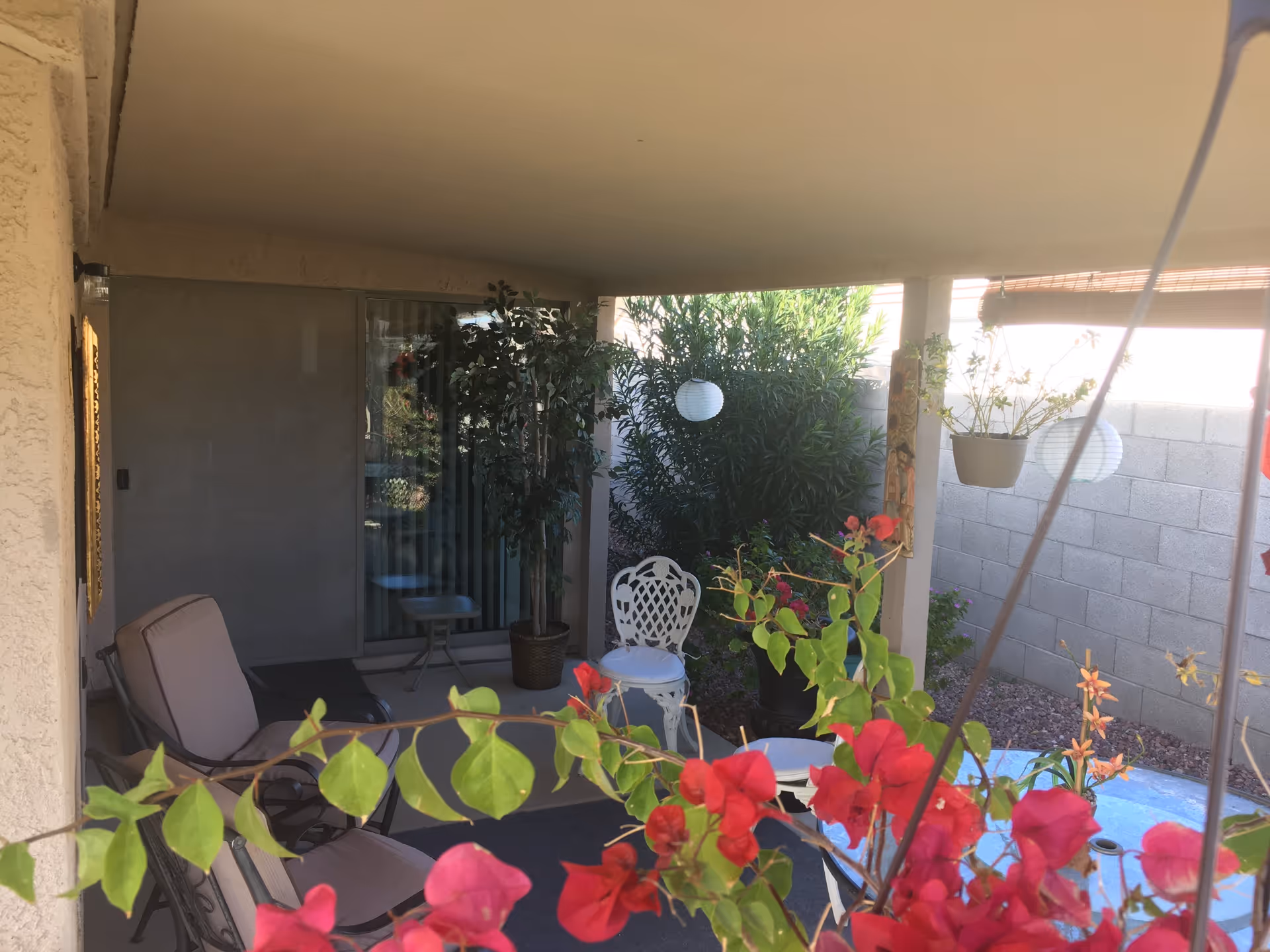 Covered patio with outdoor chairs, small tables, potted plants, hanging lanterns and bright bougainvillea flowers.