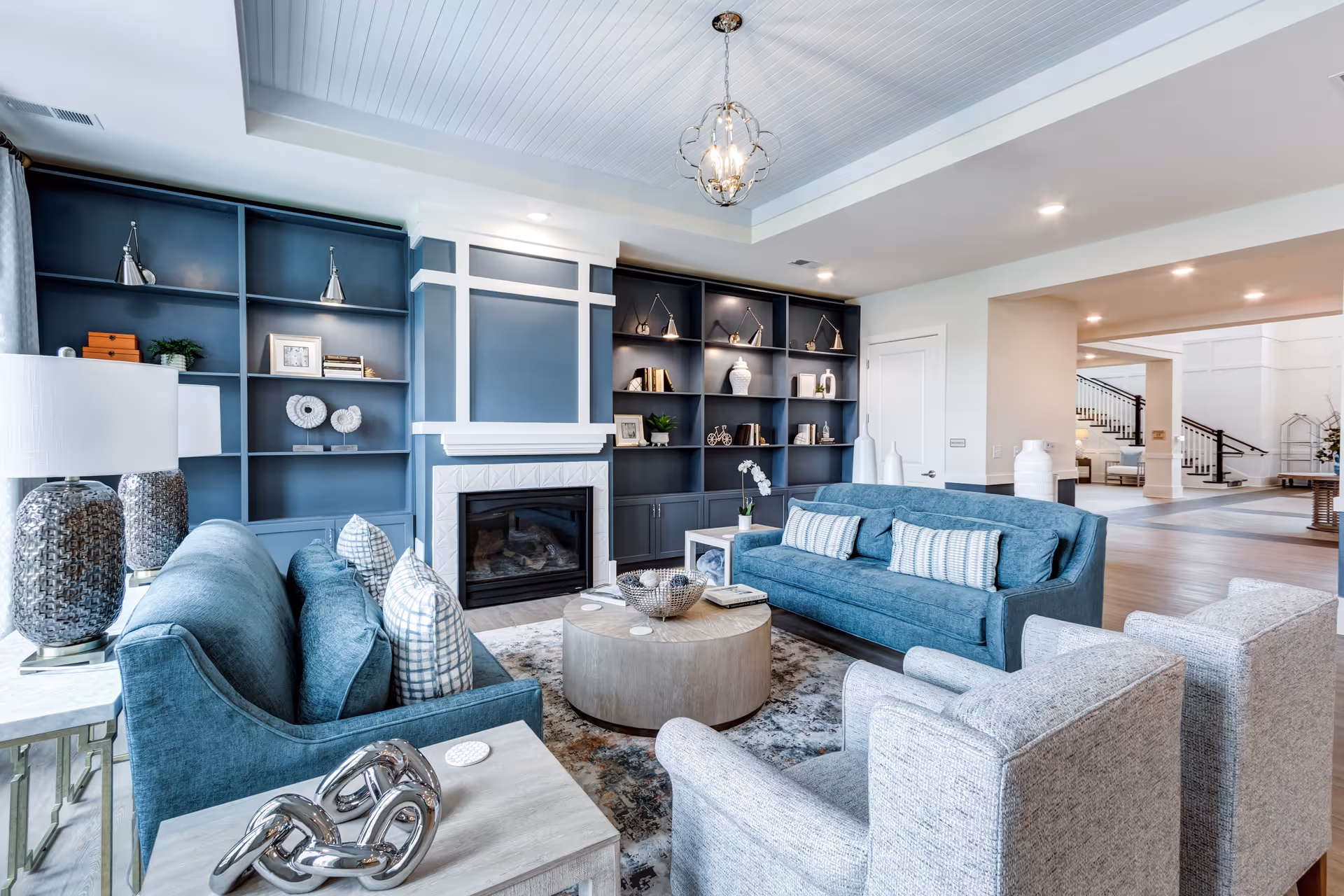 Contemporary living room with blue sofas and armchairs arranged around a round coffee table in front of built-in blue shelving and a fireplace.