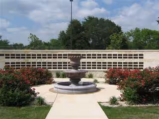 Outdoor courtyard featuring a tiered fountain, brick wall, and flowering shrubs.