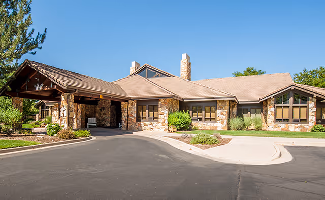 Exterior view of a stone-clad senior living facility entrance with a paved driveway.