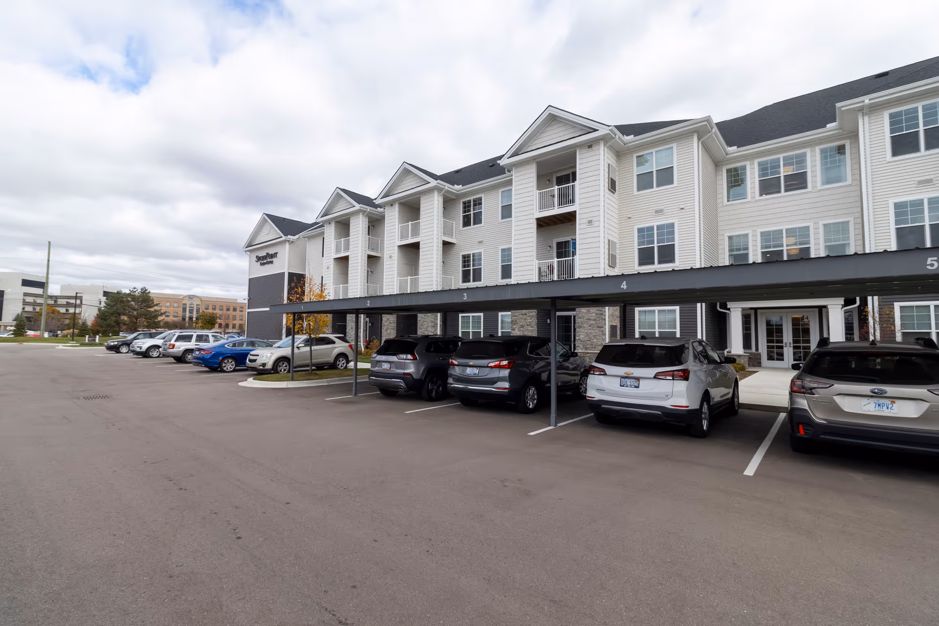 Front exterior of a three-story StoryPoint senior living building with covered parking and multiple cars in the lot.