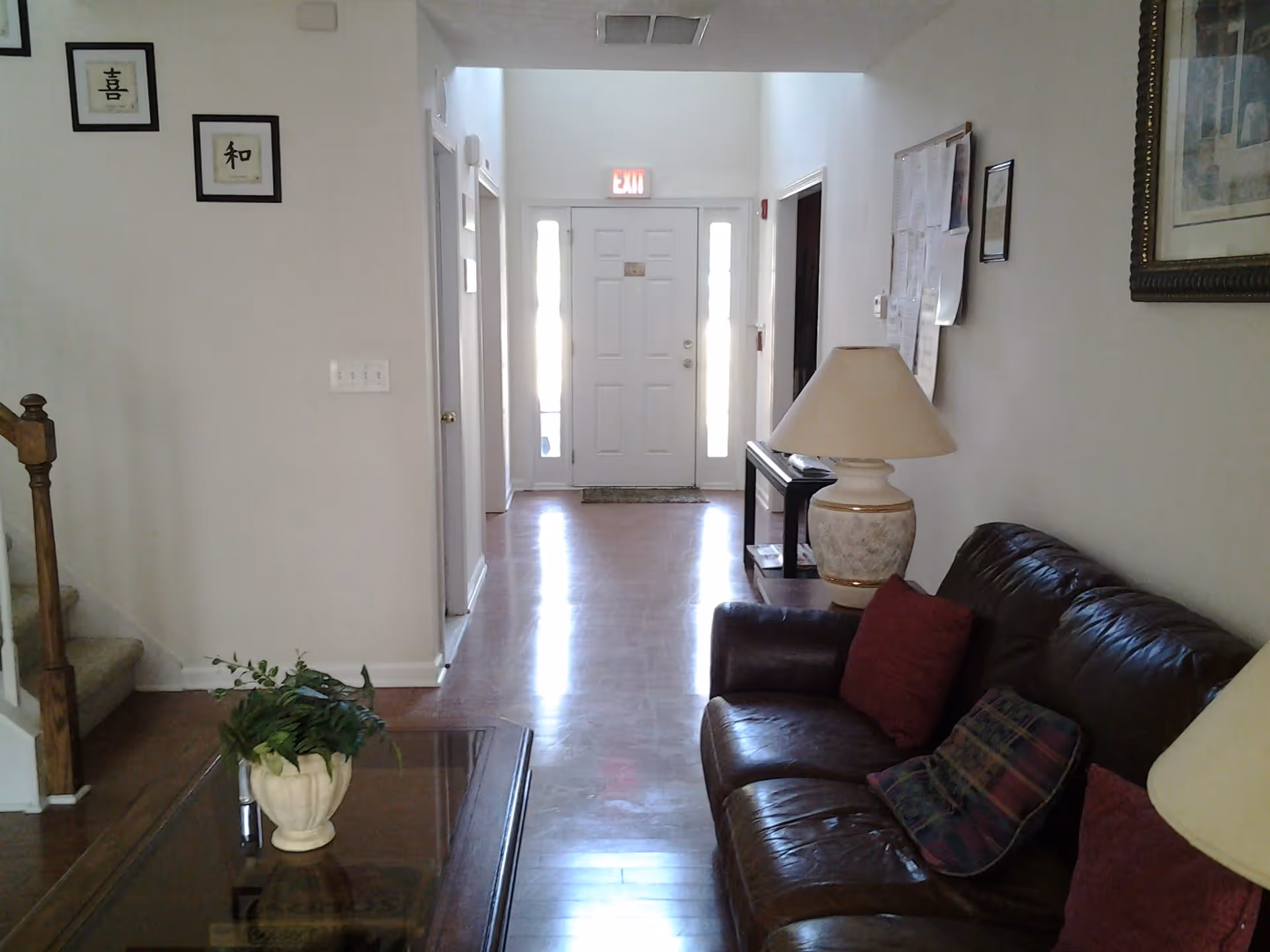 View of a living room and entry hallway with a leather sofa, coffee table, lamp, and front door at the end of the hall.