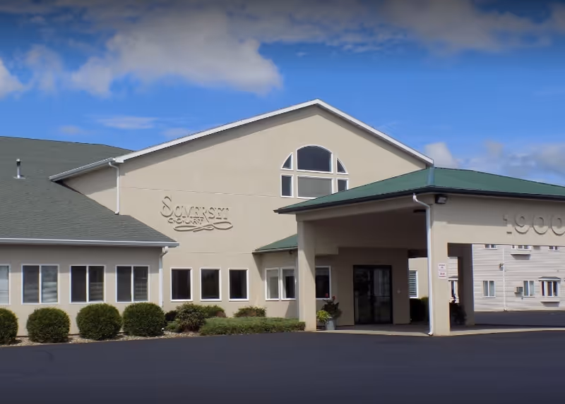 Front exterior of Somerset Court senior living facility with a covered entryway and landscaping.
