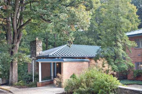 Exterior view of a brick senior living facility entrance with trees and a metal-roofed porch.