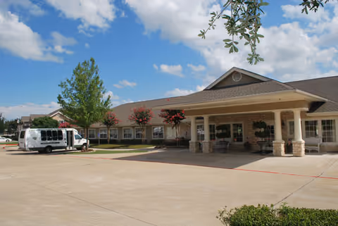 Front entrance of Brookdale Creekside senior living facility with a covered porte-cochere, parked shuttle van, and landscaped grounds under a blue sky.