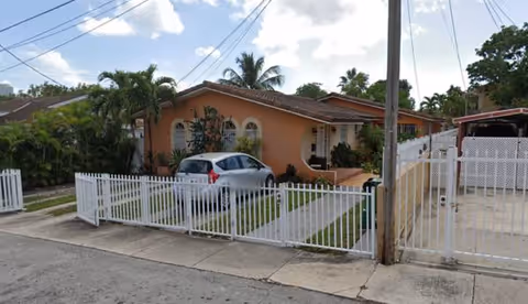 Front view of a peach-colored senior living home with a white fence and parked car.