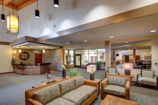 Spacious senior living facility lobby with sofas and armchairs, a reception desk, and pendant lighting.