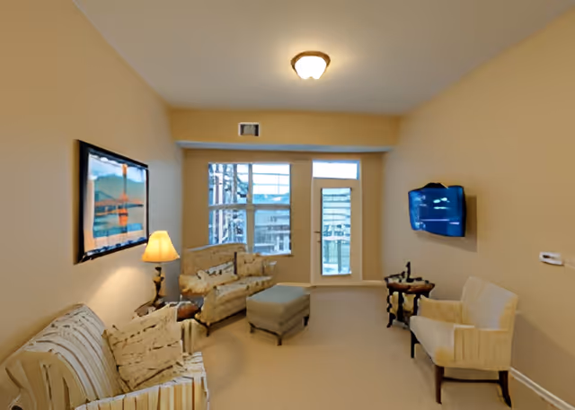 Living room with sofas, armchairs, an ottoman, a floor lamp and a wall-mounted TV facing a windowed door.