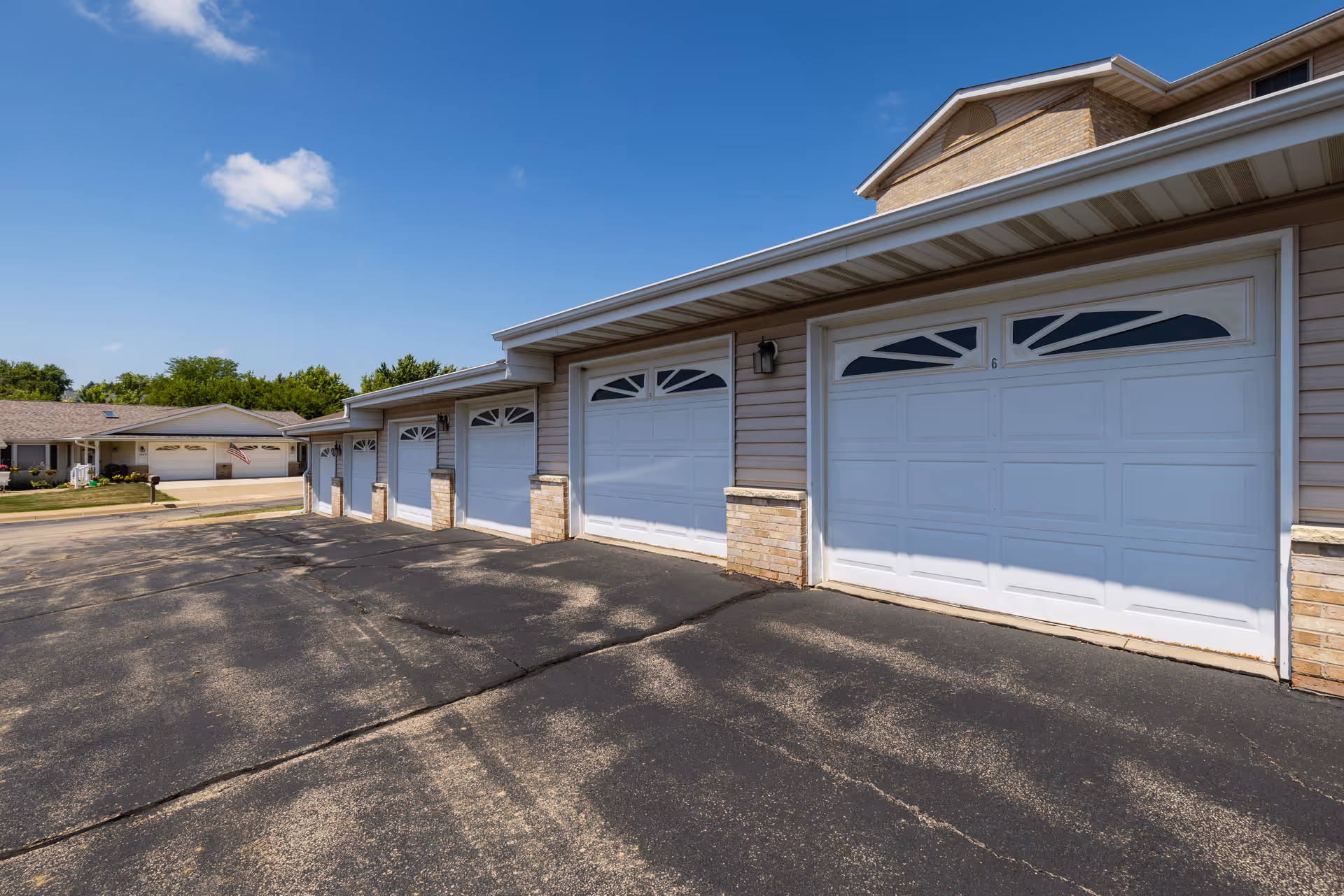 A row of attached garages with white doors and beige siding under a clear blue sky, part of a residential or senior living facility.