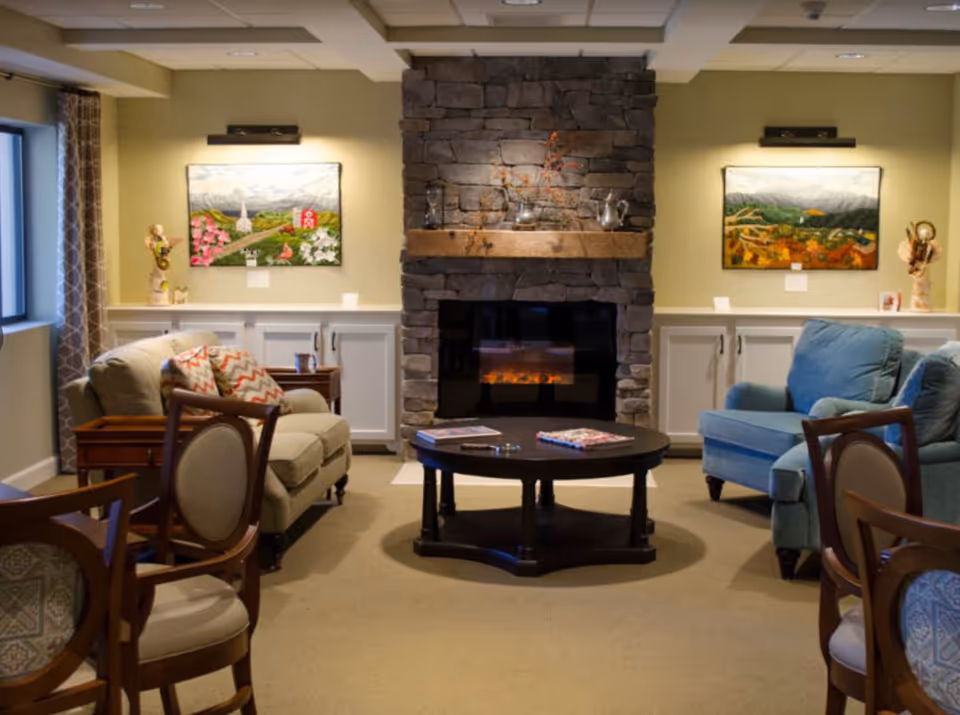 Cozy common room with a stone fireplace, armchairs, a round coffee table, and framed artwork on the walls.