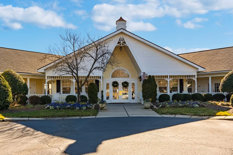 The entrance of a senior living facility with a decorated front porch and landscaped surroundings.