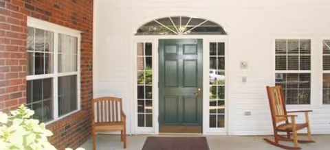 Entrance porch of a senior living facility with a green door and two wooden chairs.
