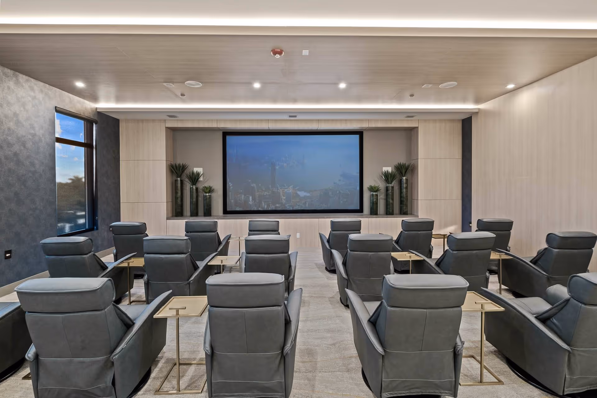 Interior screening room with multiple gray recliner seats arranged in rows facing a large projection screen.