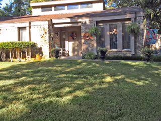 Front exterior of a single-story brick building with a grassy lawn, potted plants, and decorative wreaths at the entry.