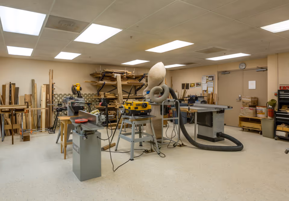 Interior woodworking shop with power tools, workbenches, stacked lumber and a dust collection system.
