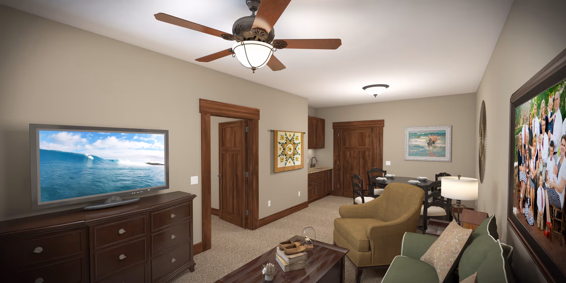 A cozy living room and dining area with beige walls and carpeted floor. The living room features a green sofa with pillows, a brown armchair, a wooden coffee table with books and decorative items, and a large flat-screen TV on a dark wooden dresser. The dining area has a round table with four chairs and place settings. The room has wooden doors and trim, a ceiling fan with light, and framed artwork on the walls.