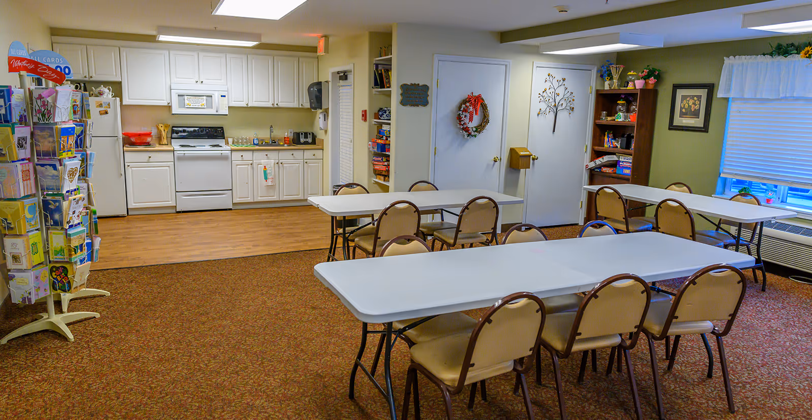 Community dining/activity room with folding tables and chairs and a kitchenette along the back wall.