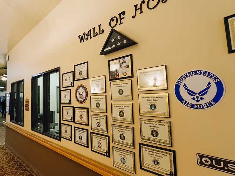 Interior hallway showing a 'Wall of Honor' with framed veteran certificates, a folded American flag display, and military emblems on the wall.