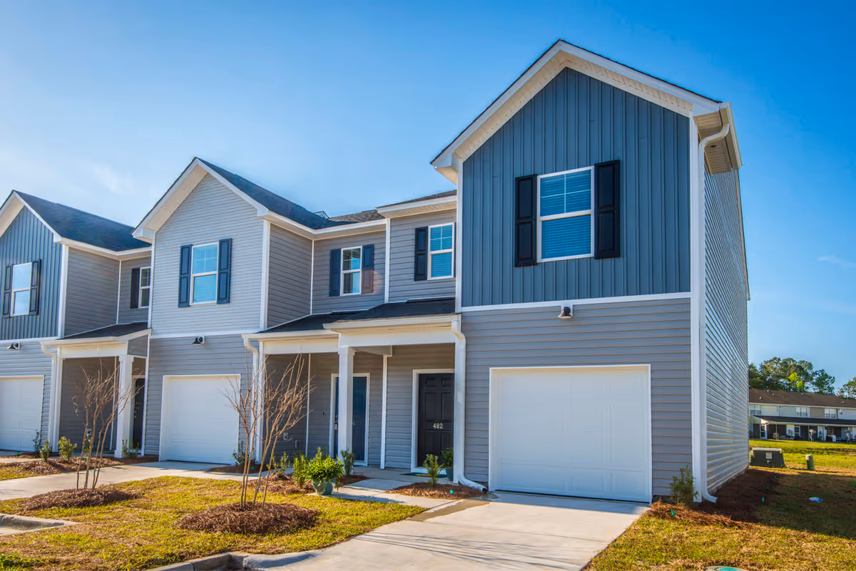 Two-story townhouse with an attached garage and small landscaped front yard under a clear blue sky.