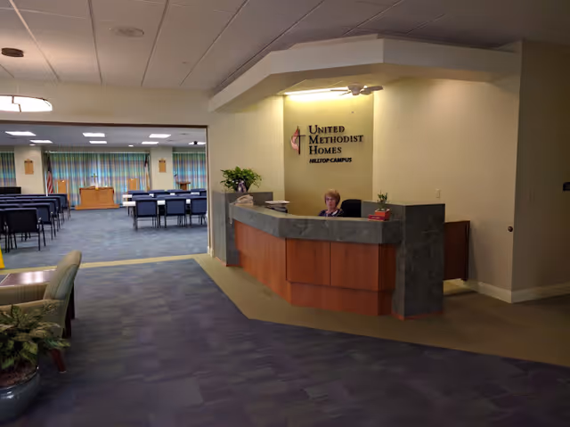 Lobby reception desk with a seated receptionist and adjacent meeting area at United Methodist Homes Hilltop Campus.