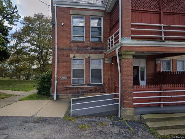 Front of a red brick building with a wheelchair ramp, porch, and multiple windows.