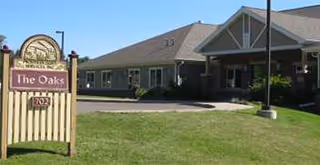 Exterior view of The Oaks Assisted Living with lawn, sign, and entrance driveway.