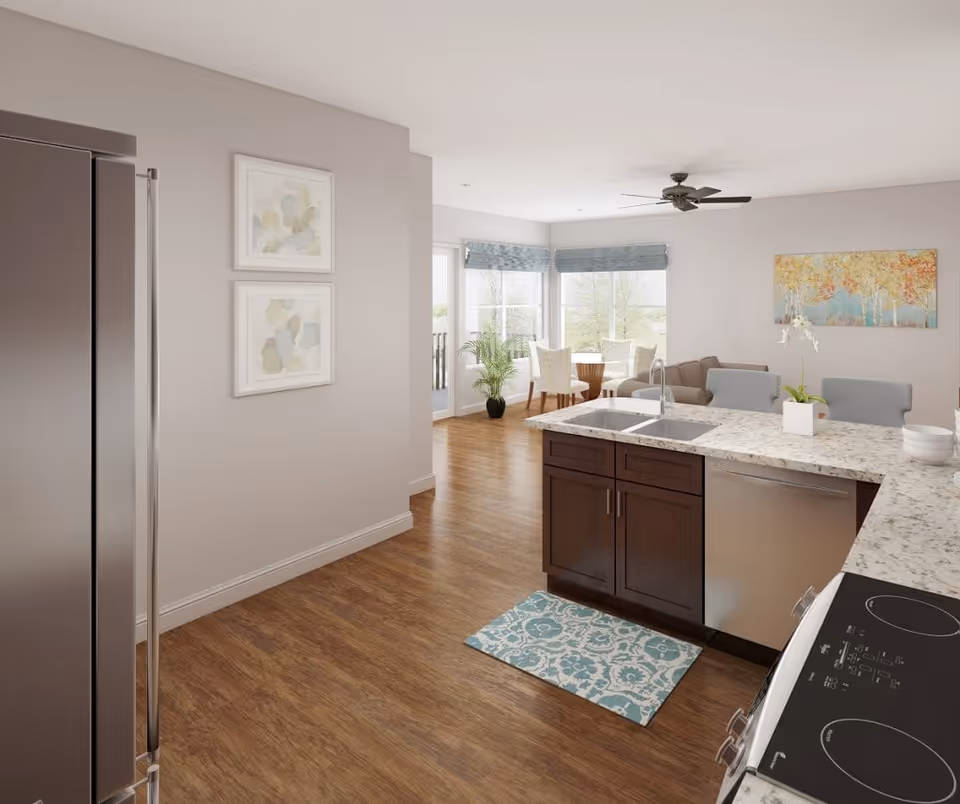 Open-plan kitchen with a marble countertop island and sink overlooking a bright dining and living area with large windows.