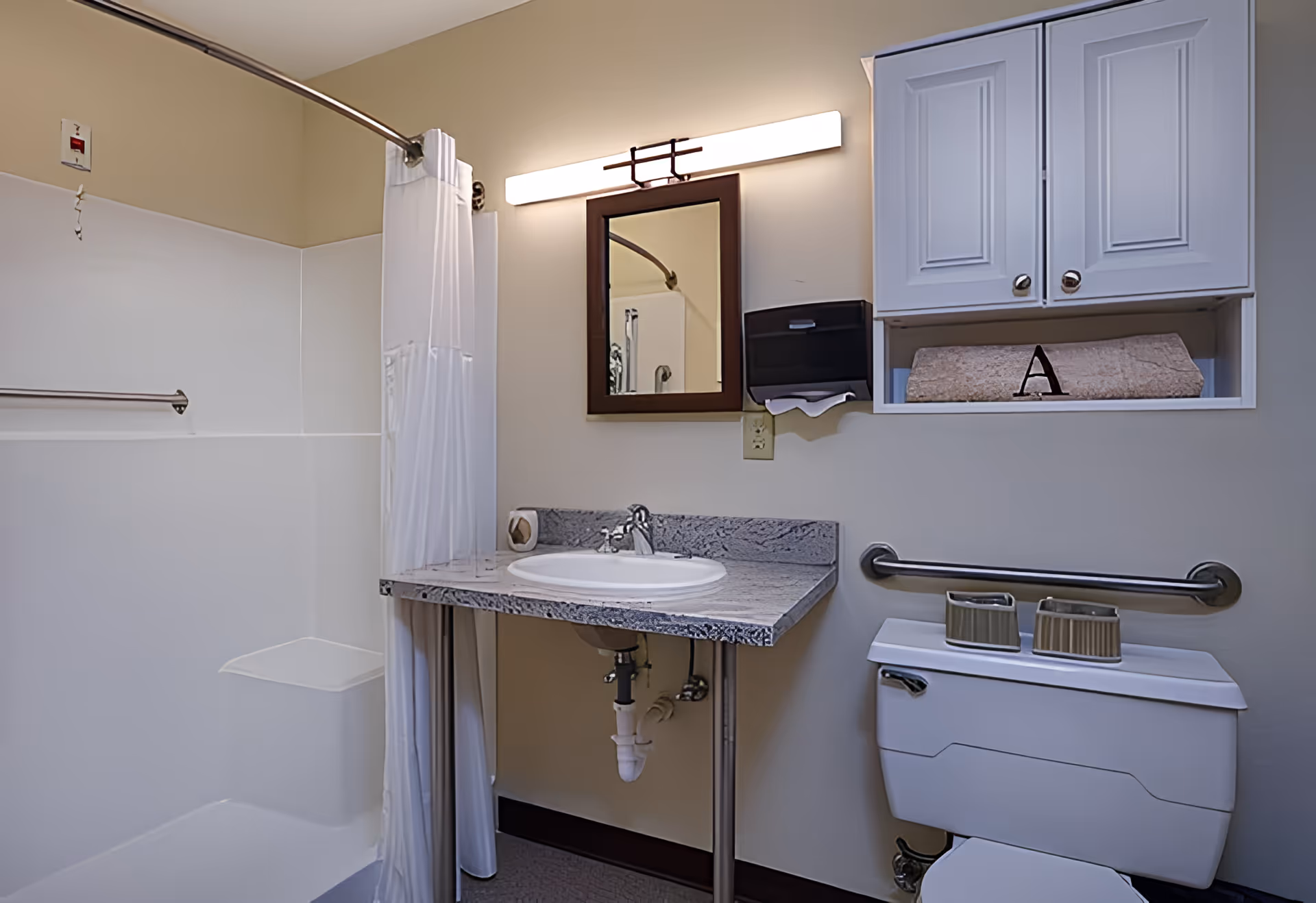 Accessible bathroom with a shower and curtain, sink with marble countertop and mirror, toilet with grab bar, and wall cabinets.
