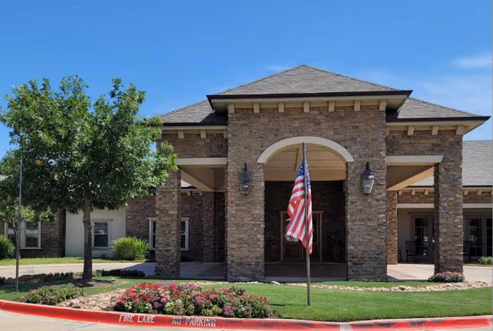 Stone front entrance of Volante Senior Living Grapevine with flag and landscaped grounds