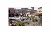 A landscaped courtyard with pathways, shrubs, a small pond and decorative elements between brick buildings.