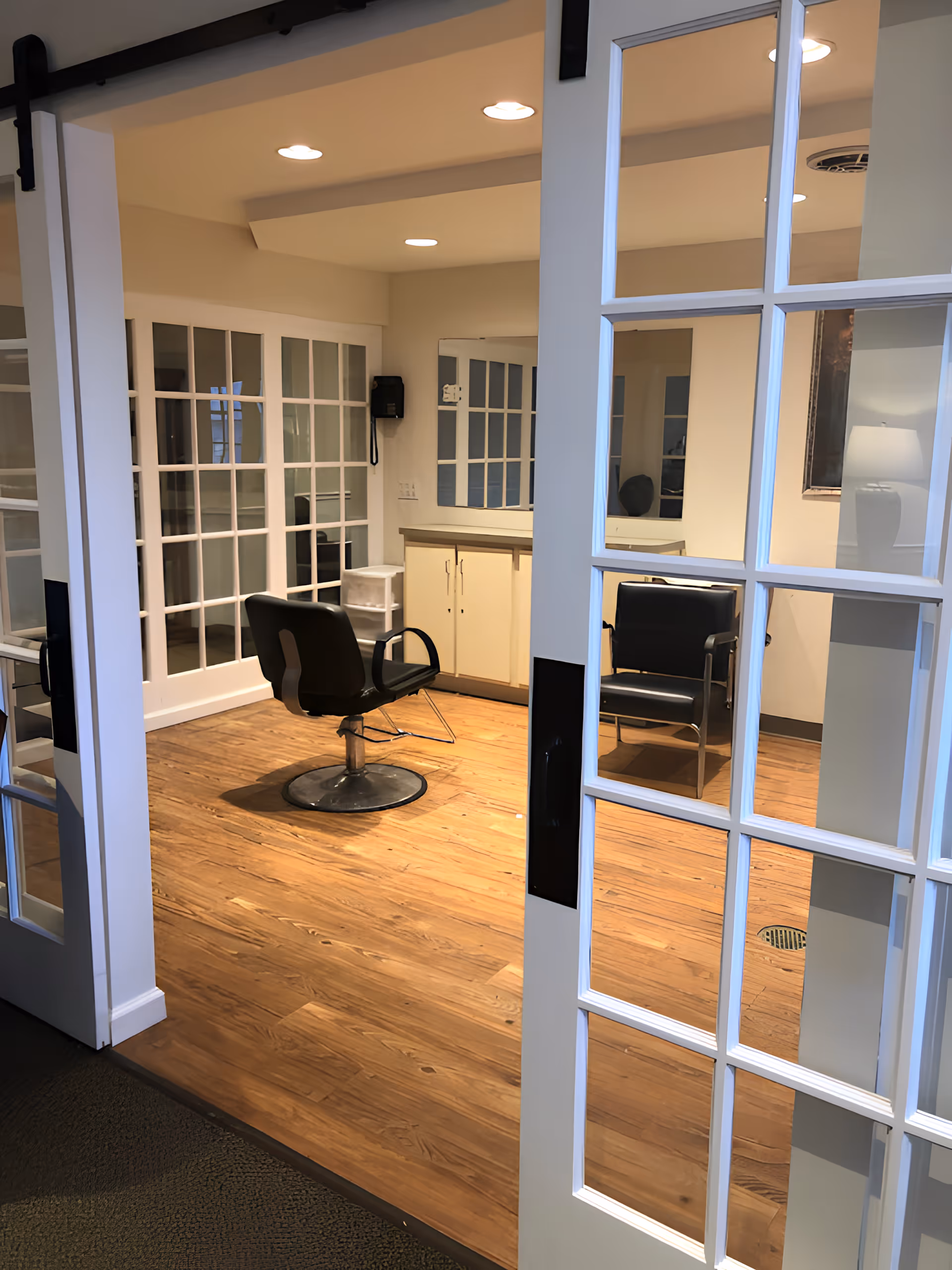 Glass-paneled doors open to an interior salon area with styling chairs, mirrors, cabinetry, and wood floors.