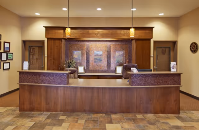 Reception desk area with a wooden front desk, pendant lights, framed artwork and tiled floor in a memory care facility.
