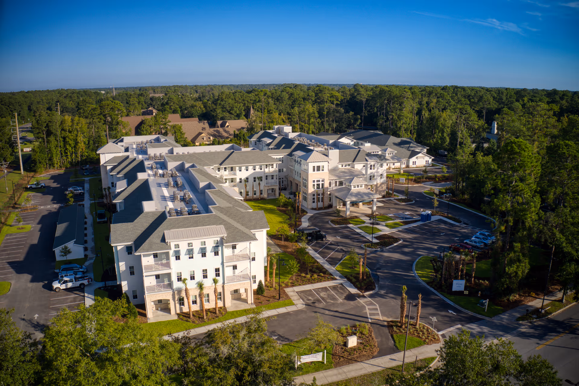 Aerial view of a large multi-story senior living facility surrounded by trees with parking lots and driveways.