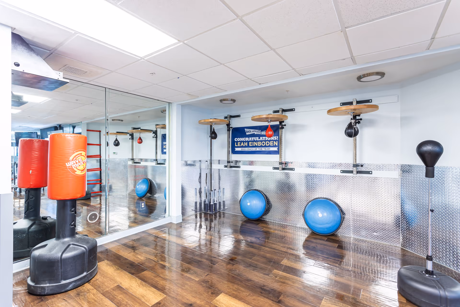 Small fitness room with freestanding punch bags, wall-mounted speed bag platforms, exercise balls, and a mirrored wall.