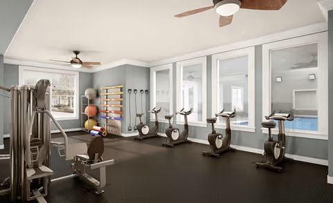Bright indoor fitness room with exercise machines, stationary bikes, weight rack, stability balls and ceiling fans.