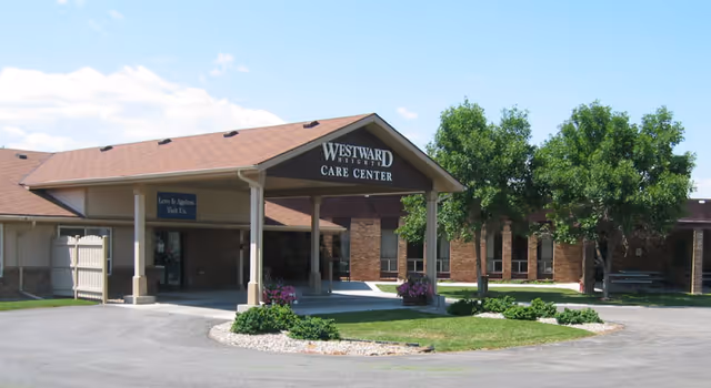 Exterior view of Westward Heights Care Center building with a covered entrance, a driveway, green lawn, and trees under a clear blue sky.