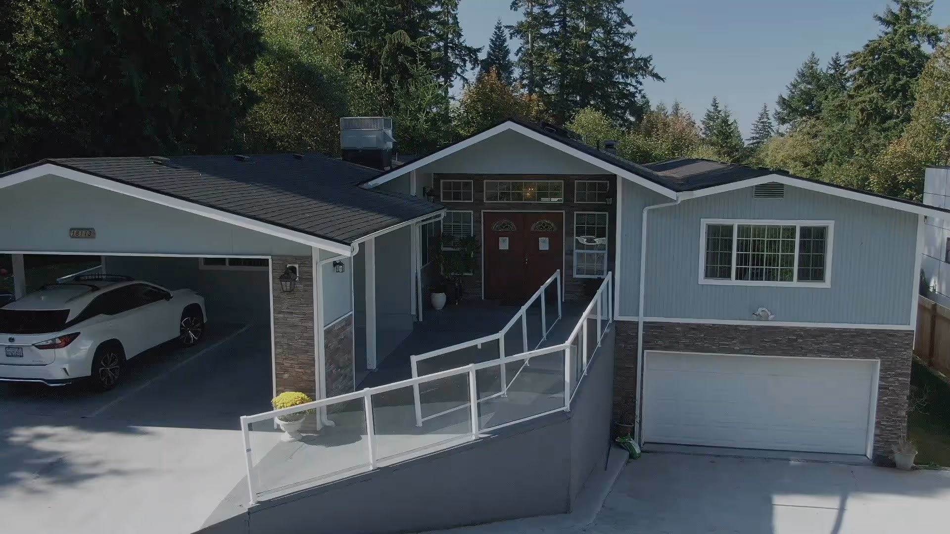 Front exterior of a single-story house with a ramp leading to double doors, a two-car garage, and a parked white SUV.