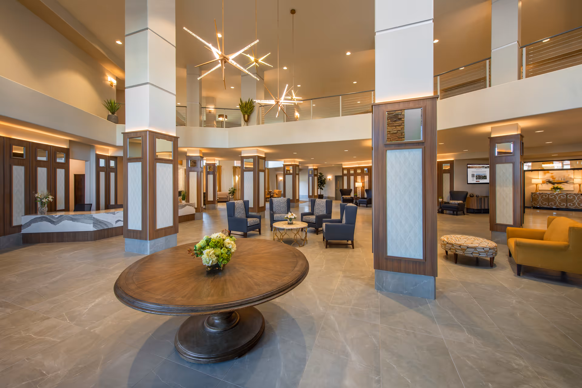 Spacious two-story lobby with a round center table, seating areas, decorative columns, and modern chandeliers.