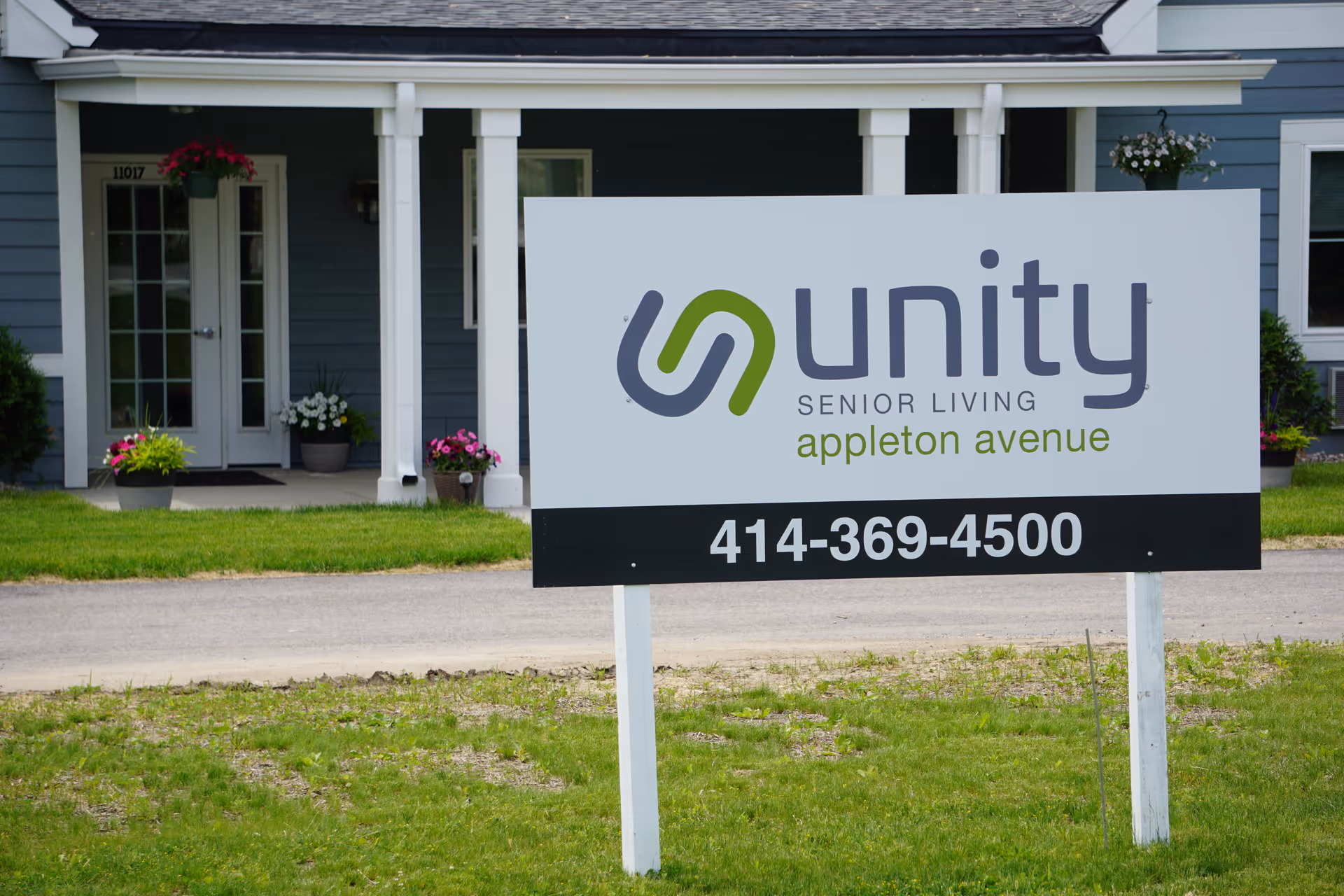 A large Unity Senior Living sign with phone number stands on the lawn in front of the facility entrance.