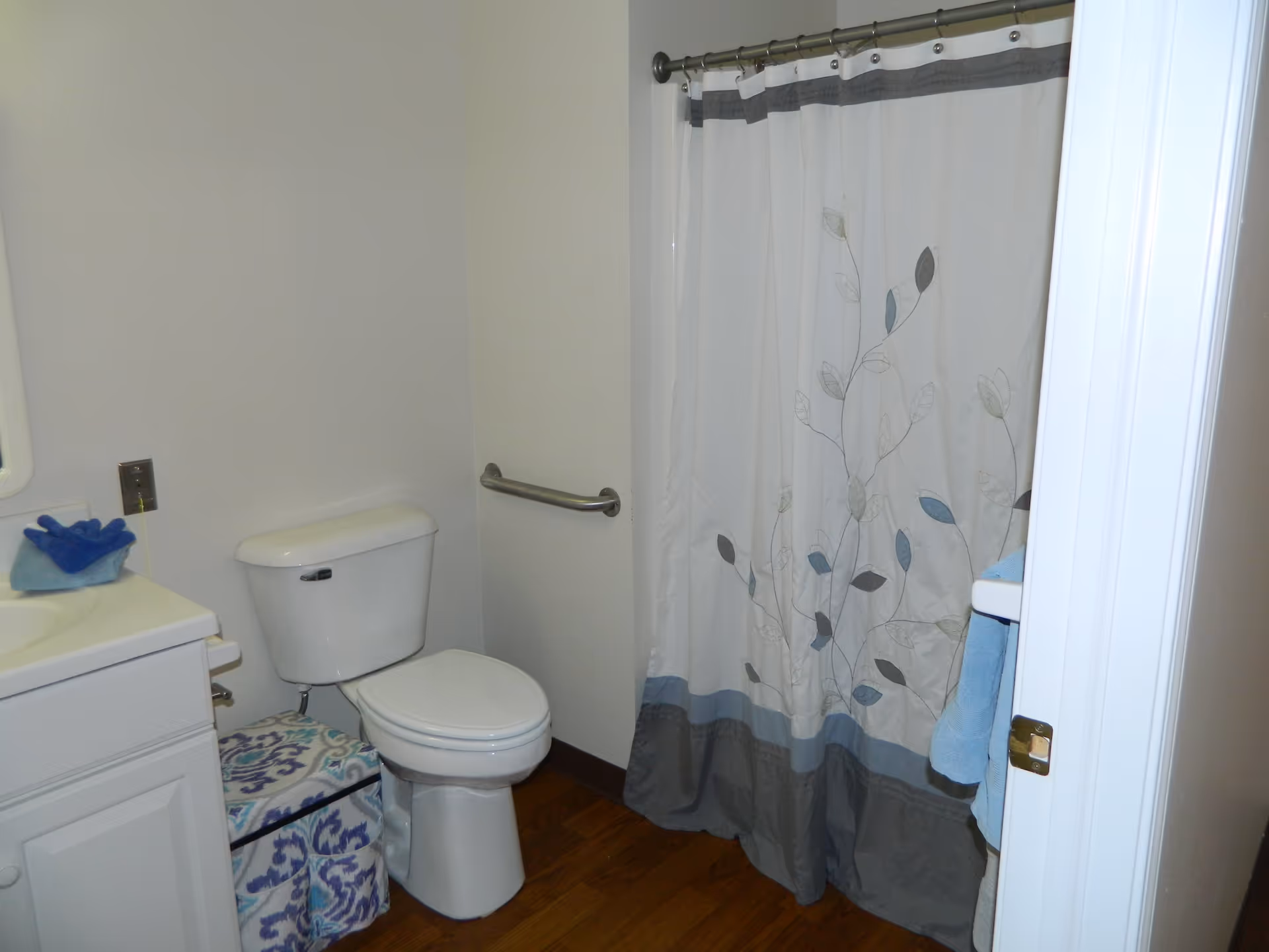 Small bathroom with a toilet, white vanity, grab bar and a floral-patterned shower curtain.