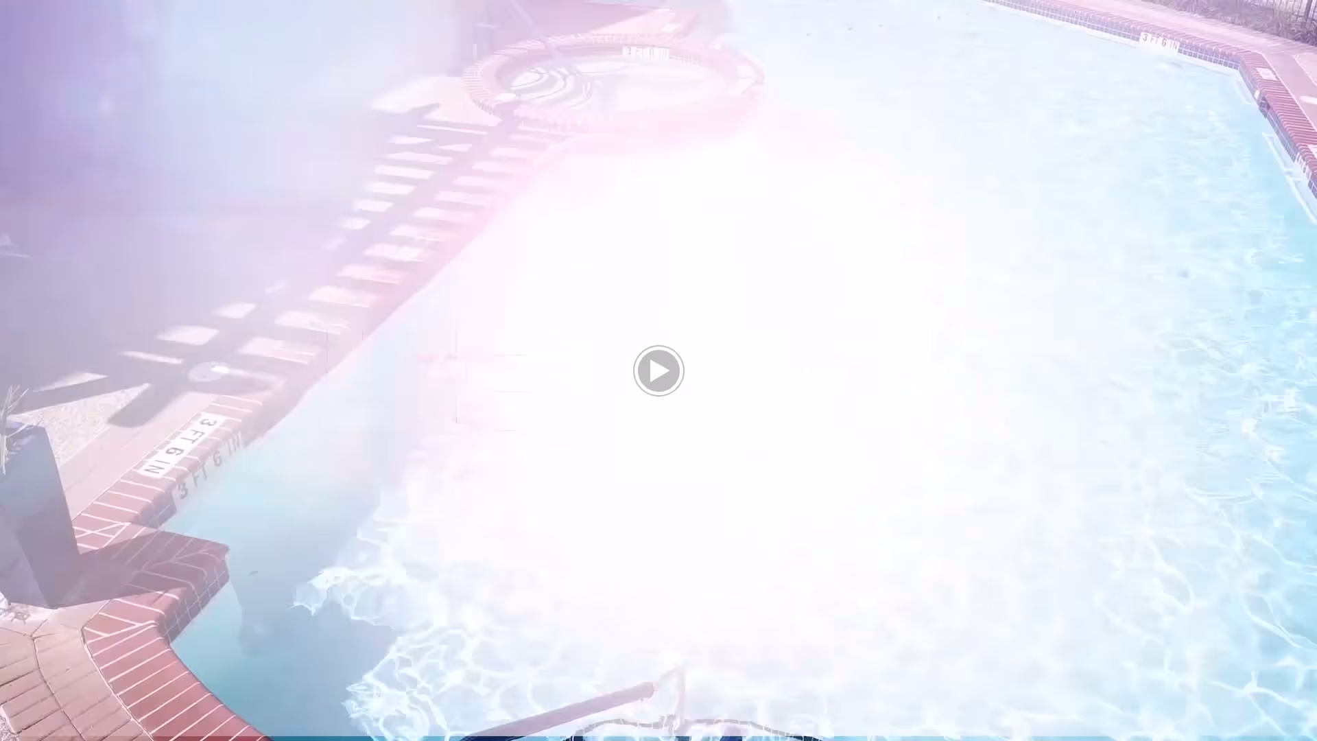 Outdoor swimming pool with clear blue water surrounded by a brick border and a hot tub in the background.