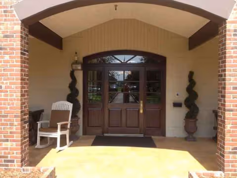 Brick building entrance with double wooden doors, arched top, and decorative spiral topiaries on each side.