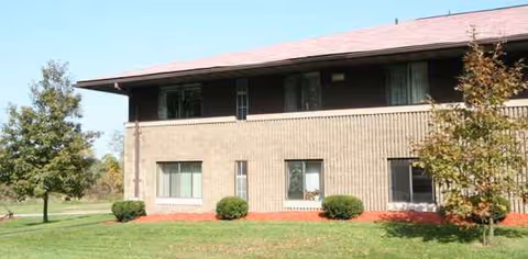 Two-story brick senior living facility with a grassy lawn and trees.