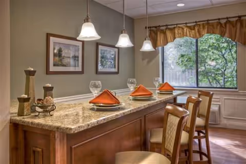 Interior dining area with a granite-topped bar set with place settings and bar stools beneath pendant lights near a window.