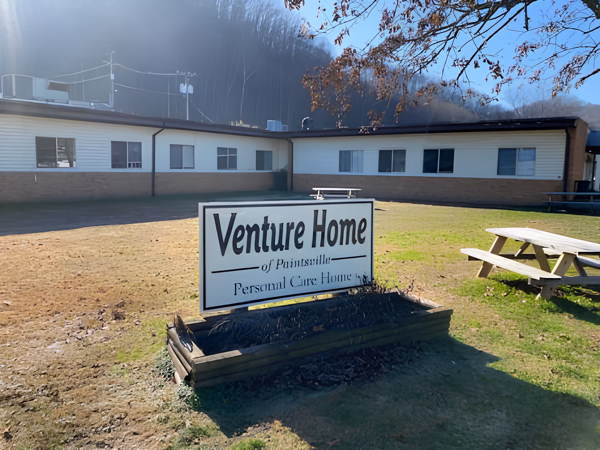 Exterior view of the Venture Home building with a lawn, picnic table, and a prominent sign reading 'Venture Home'.