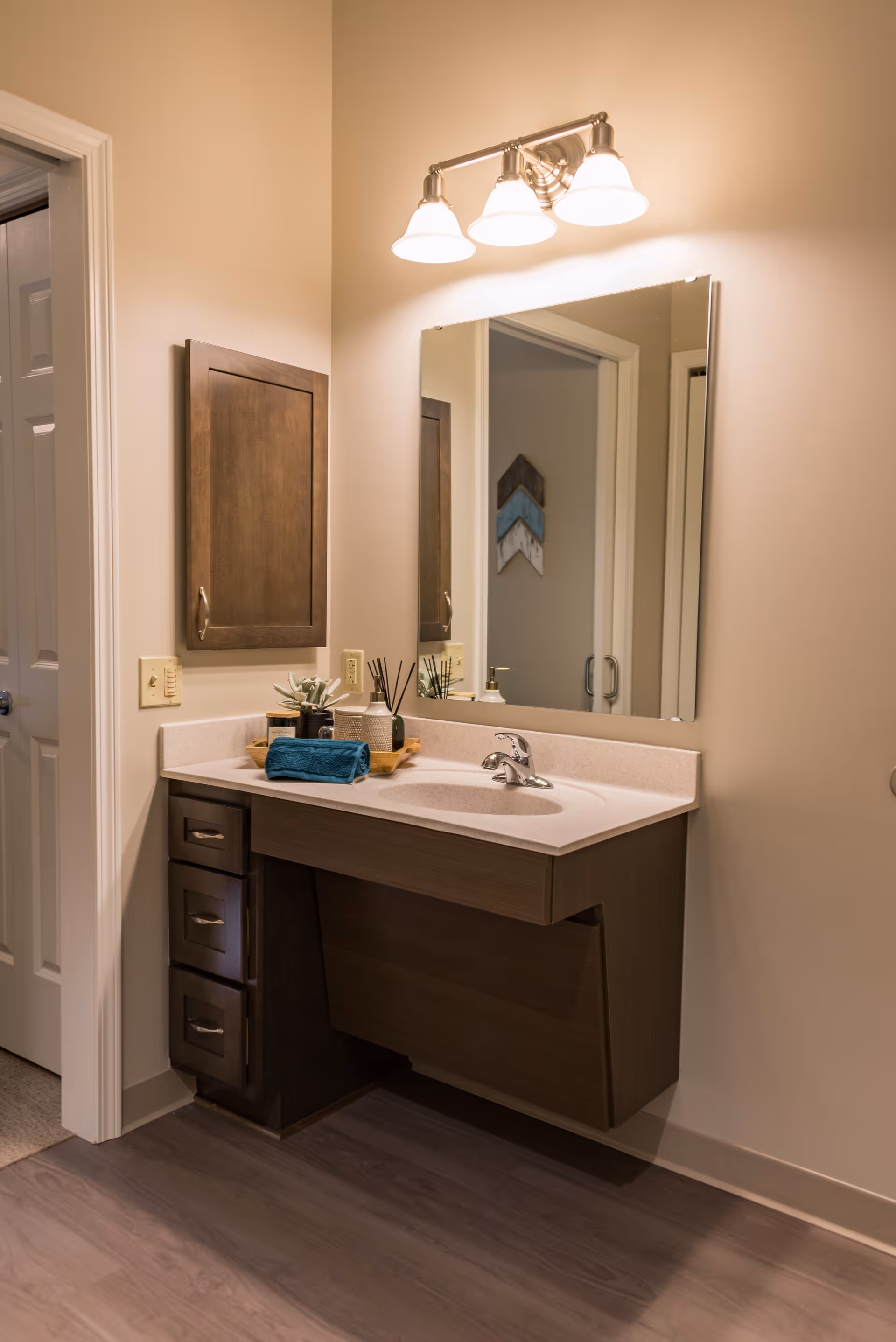 A bathroom vanity with a sink, mirror, wall cabinet, overhead lights and decorative items on the countertop.